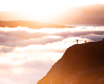 Silhouette of a person standing triumphant on a mountain cliff amidst the breathtaking morning clouds. HD wallpaper