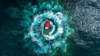 Red motor boat making spiral waves on turquoise ocean in aerial view, shot by drone. HD wallpaper