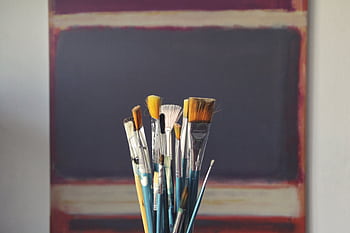 A set of paintbrushes in front of an abstract canvas, reflecting creativity and inspiration. HD wallpaper