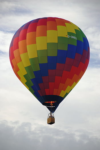 Vibrant rainbow hot air balloon against a cloudy sky, symbolizing adventure and dom. HD phone wallpaper
