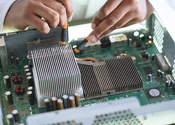 Close-up of a technician repairing a computer motherboard, focusing on microprocessor and heat sink. HD wallpaper
