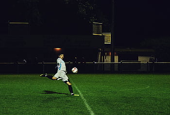 Dynamic action shot of a soccer player kicking the ball during a night game in Somerset, England. HD wallpaper