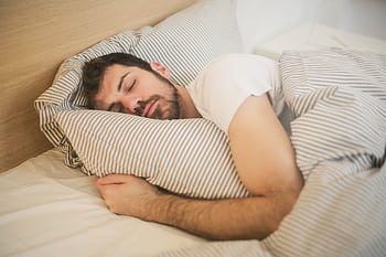 Man sleeping peacefully on striped bedding, embracing relaxation and comfort. HD wallpaper