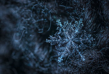 Detailed macro of a single snowflake resting on a textured dark surface, highlighting its crystalline structure. HD wallpaper