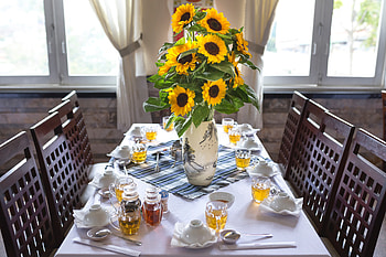 Cheerful Sunflowers in Asian Vase, sunflower arrangement, windows, tablecloth, 5760x3840, cups, chairs, spoons, brown, glasses, beverages, curtains, table, asian vase, sunshine, dishes, place setting, green, yellow HD wallpaper