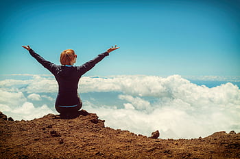 A woman enjoys a scenic view atop a cliff in Kula, Hawaii, surrounded by clouds and blue sky. HD wallpaper