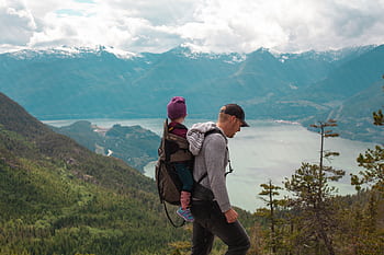 A father carries his child on a scenic mountain trail, embracing adventure and parenthood. HD wallpaper