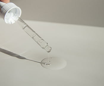 Close-up of a cosmetic pipette releasing serum onto a surface with soft sunlight. HD wallpaper