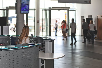 A bustling office reception area with people walking and a receptionist at a modern desk. HD wallpaper