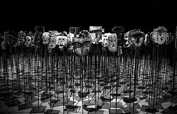 An artistic display of wooden masks on poles, set in a dimly lit theater. HD wallpaper