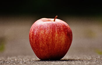 A vibrant red apple resting on a textured outdoor surface, showcasing natural beauty and freshness. HD wallpaper