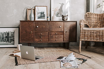 A cozy home office interior featuring a rustic wooden cabinet, wicker chair, and open laptop. HD wallpaper