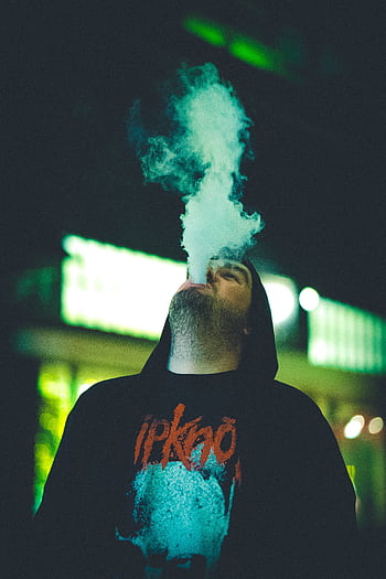 A young man exhales vapor in a neon-lit environment, creating a dramatic ambiance. HD phone wallpaper