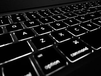 Black and white close-up of backlit keyboard, highlighting the glowing keys. HD wallpaper