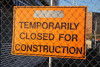 Orange sign behind fence reading 'Temporarily Closed for Construction' at site. HD wallpaper