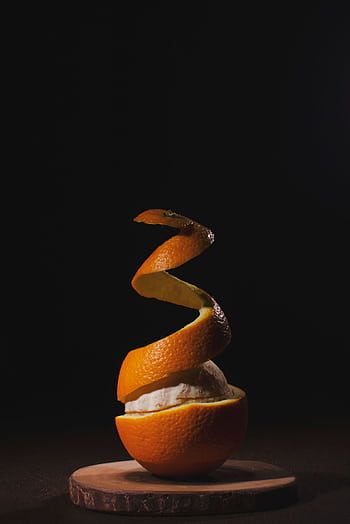 A creatively peeled orange with spiral skin on a wooden board against a dark background. HD phone wallpaper