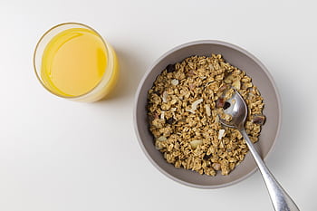 A top view of granola in a bowl with a spoon and a glass of orange juice on a white background. HD wallpaper