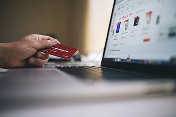 Person holding a credit card while shopping online on a laptop, indicating ecommerce transactions. HD wallpaper