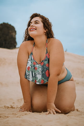 A cheerful woman poses confidently on a sandy beach under a clear blue sky, showcasing summer vibes and body positivity. HD phone wallpaper