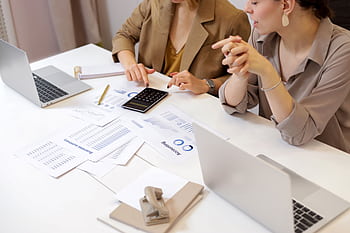 Two professionals collaborating on financial documents in a modern office setting. HD wallpaper