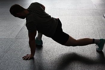 Silhouette of a man executing a stretching routine in a dim gym environment. HD wallpaper