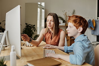 A mother and her son attentively engaged in online learning at home on a computer. HD wallpaper