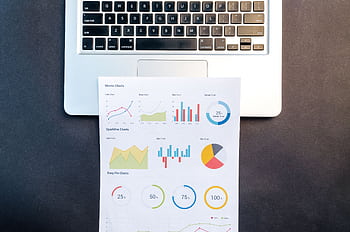 Top-down view of a laptop keyboard and colorful printed charts on a desk. HD wallpaper