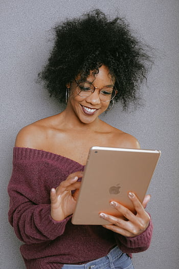 A young woman with curly hair smiling while using a tablet indoors. HD phone wallpaper