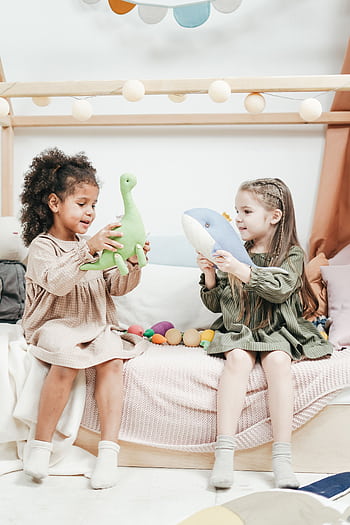 Two young girls playing happily with stuffed toys indoors in a cozy setting. HD phone wallpaper