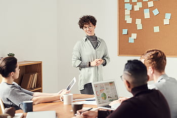 Diverse team discussing ideas during an office meeting with charts displayed on laptops. HD wallpaper