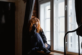 A woman sits by a window, lost in deep thoughts and moody light. HD wallpaper