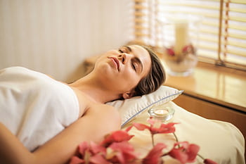 Woman enjoying a relaxing spa day with flowers and candles indoors. HD wallpaper