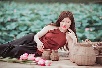 A young woman poses gracefully amidst baskets and lotus flowers in a serene garden setting. HD wallpaper