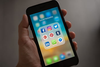A smart displaying various social media icons held in a hand, showcasing modern communication apps. HD wallpaper