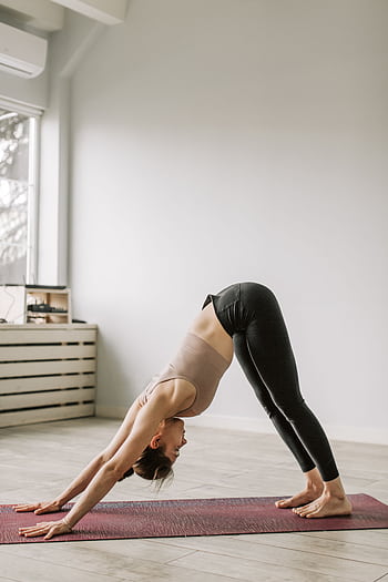 Adult woman in a downward facing dog yoga pose on a mat indoors during daytime. HD phone wallpaper