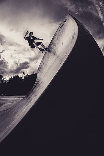 A skateboarder rides up a ramp with dramatic flair and energy against a stormy sky. HD phone wallpaper