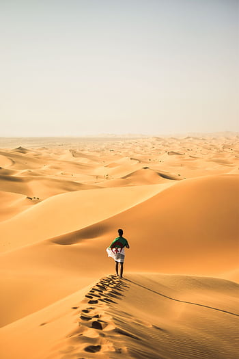A solitary traveler walks across the vast sand dunes of the Sahara Desert in Algeria. HD phone wallpaper