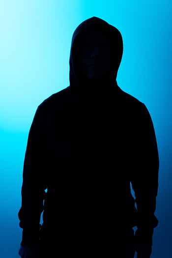 Silhouette of a hooded figure backlit by eerie blue light, creating a mysterious atmosphere. HD phone wallpaper