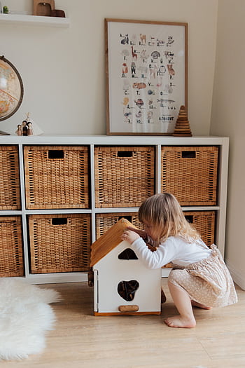 A cute toddler plays with a dollhouse in a cozy room with wooden storage baskets. HD phone wallpaper