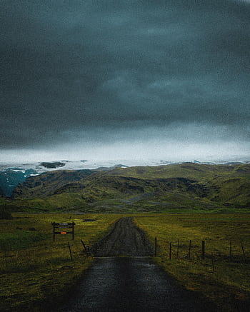 Moody Icelandic landscape with a dramatic stormy sky, lush greenery, and a winding road. HD phone wallpaper