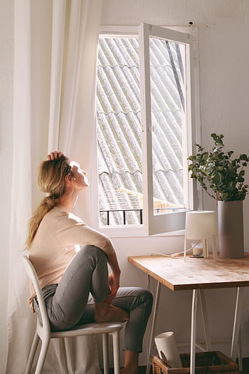 A serene moment as a woman enjoys sunshine near a window in a cozy interior setting. HD phone wallpaper