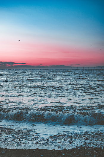 A tranquil ocean scene at dawn showcasing waves under a dramatic pink and blue sky. HD phone wallpaper