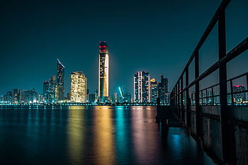Stunning Abu Dhabi skyline at night with city lights reflecting off the calm waterfront. HD wallpaper