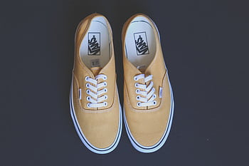 Pair of stylish yellow sneakers on a black background showcasing fashion and footwear design. HD wallpaper