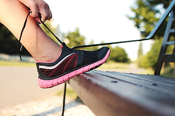 A woman laces her sneakers on a park bench, preparing for a run outdoors. HD wallpaper