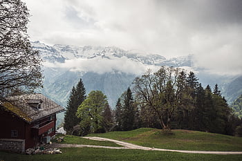 Peaceful mountain scene featuring a rustic house and snow-capped peaks. HD wallpaper