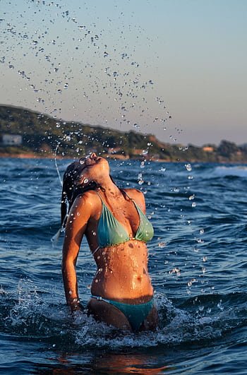 A woman in a bikini enjoying the ocean waves at sunset, creating a vibrant splash. HD phone wallpaper