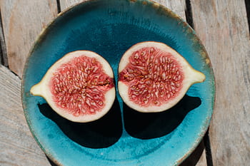 Close-up of a fresh ripe fig sliced in half on a vibrant blue plate outdoors. HD wallpaper