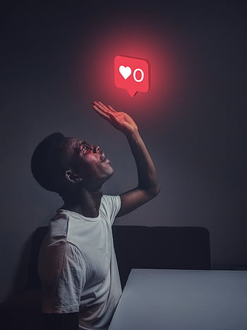 A man sits indoors reaching towards a glowing social media notification icon. HD phone wallpaper