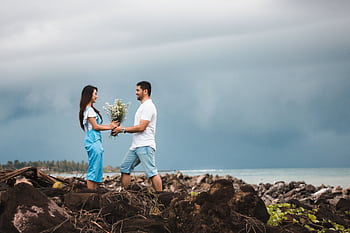 A couple enjoys a romantic moment by the rocky seashore under a cloudy sky. HD wallpaper